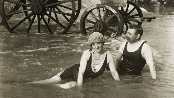 Paar in einteiligen Badeanzügen im flachen Wasser vor einem Badekarren um 1910. © picture alliance / akg-images Foto: akg-images