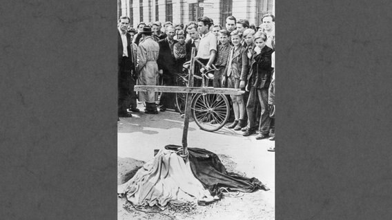 Menschen stehen am 17. Juni 1953 in Ostberlin vor einem Holzkreuz, das an der Stelle errichtet wurde, an der ein Demonstrant von einem sowjetischen Panzer überrollt worden war. © picture-alliance / akg-images 