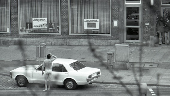 Ein Mann in Badehose steht vor einem weißen Ford, der vor einem Gebäude parkt. © Staatsarchiv Hamburg Plankammer 