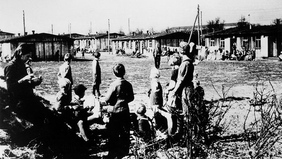 Kinder und Erwachsene in einem Flüchtlingslager in Schleswig-Holstein 1945. Kinder und Erwachsene in einem Flüchtlingslager in Schleswig-Holstein 1945. © dpa - Report
