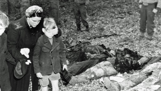 Eine deutsche Mutter schirmt die Augen ihres Sohnes ab, während sie mit anderen Zivilisten an Leichen vorbeigeht, die nach dem Zweiten Weltkrieg aus einem Massengrab exhumiert wurden. © National Archives and Records Administration, College Park 