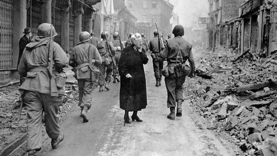 US-Truppen marschieren am Ende des Zweiten Weltkriegs in eine zerstörte Stadt ein. © dpa - Bildarchiv 
