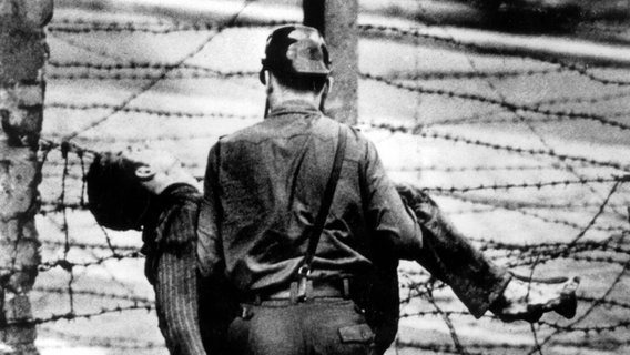 Ein Grenzsoldat trägt den bei seinem Fluchtversuch an der Berliner Mauer erschossenen Peter Fechter am 17. August 1962 davon. © picture alliance Foto: picture alliance
