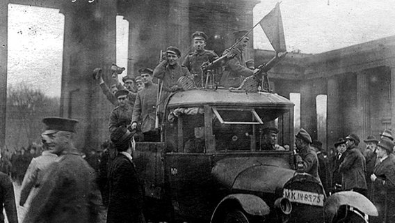 Soldaten mit einer roten Fahne fahren am 9. November 1918 durch das Brandenburger Tor. © picture-alliance / akg-images 