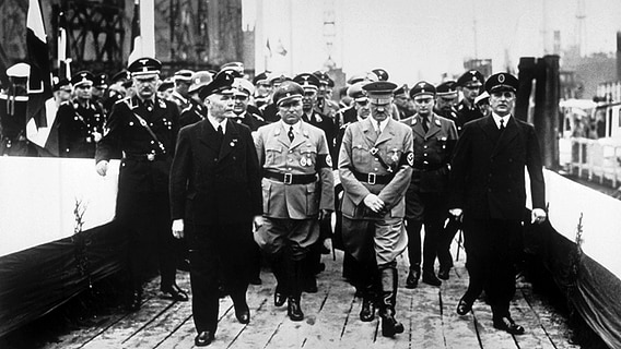 Adolf Hitler am 5. Mai 1937 auf dem Weg zur Taufkanzel in Begleitung von Robert Ley und Blohm junior. Adolf Hitler am 5. Mai 1937 auf dem Weg zur Taufkanzel in Begleitung von Robert Ley und Blohm junior. © picture-alliance / akg-images Foto: akg-images