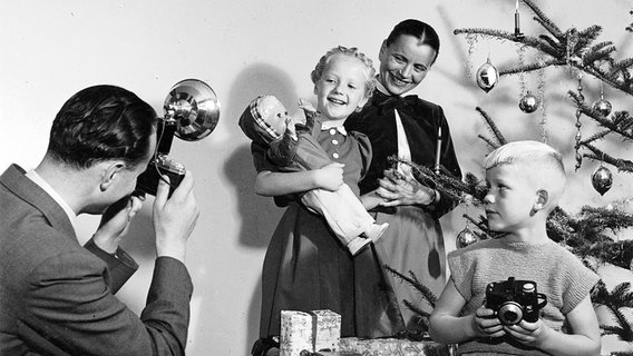Ein Vater fotografiert seine Kinder mit Geschenken vor dem Weihnachtsbaum, Fotografie 50er- bis 60er-Jahre. © Kurt Röhrig/Helga Lade Foto: Kurt Röhrig