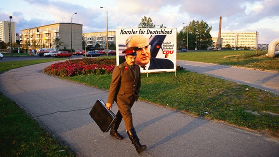 In einem Schweriner Plattenbaugebiet hängt ein Wahlplakat von Helmut Kohl. Davor geht ein Soldat die Straße entlang. (Fotograf: Kurt W. Hamann) © Kurt W. Hamann Foto: Kurt W. Hamann