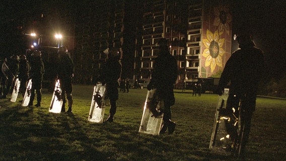 Polizisten in schwerer Ausrüstung und mit Schilden schirmen das inzwischen geräumte und teilweise abgebrannte Asylbewerberheim in Rostock-Lichtenhagen in der Nacht zum 27. August 1992 ab. © picture alliance / ZB Foto: Jens Kalaene