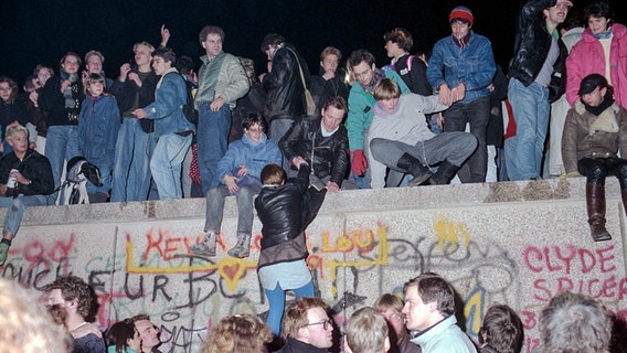 Menschen feiern am 10. November 1989 vor und auf der Mauer in Berlin den Mauerfall. © picture-alliance/ ZB Foto: Peter Zimmermann