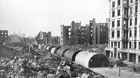 Vor Ruinen ausgebombter Wohnhäuser in Hamburg stehen Behelfsheime, sogenannte Nissenhütten. Vor Ruinen ausgebombter Wohnhäuser in Hamburg stehen Behelfsheime, sogenannte Nissenhütten. © picture-alliance/ dpa Foto: Ulrich Mohr