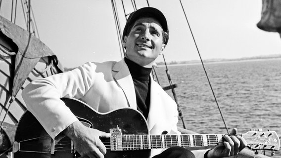 Sänger Freddy Quinn mit Gitarre singt in den 50er-Jahren auf einem Schiff "Heimweh". © picture alliance/United Archives | Siegfried Pilz 