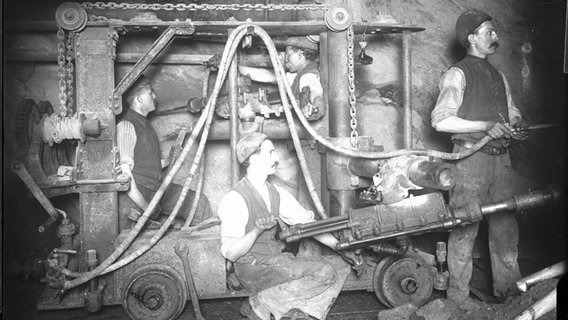 Bergarbeiter sind an einer Stollenwand mit Bohrarbeiten beschäftigt, historische Aufnahme von 1910. Bergarbeiter sind an einer Stollenwand mit Bohrarbeiten beschäftigt, historische Aufnahme von 1910. © Oberharzer Bergwerksmuseum