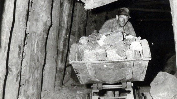 Ein Bergarbeiter schiebt einen Förderwagen aus einem Stollen. © Bergbaumuseum Bad Grund 