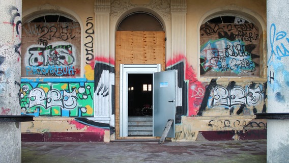 Eine Metalltür in der Graffiti-verschmierten Eingangsfront der Villa Baltic in Kühlungsborn steht offen. © NDR Foto: Daniel Sprenger