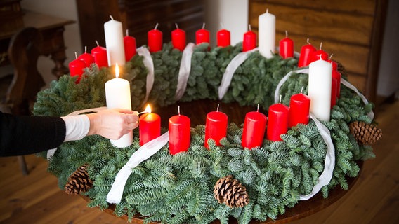 Eine Frau zündet in einer Stube der Stiftung Rauhes Haus in Hamburg die ersten Kerzen eines Adventskranzes mit 24 Kerzen an. © picture alliance / dpa Foto: Daniel Reinhardt