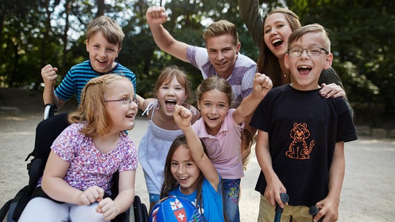 Eine Gruppe von Kindern und ein junger Mann schauen in die Kamera und strecken die Arme in die Höhe. © Lebenshilfe Foto: David Maurer