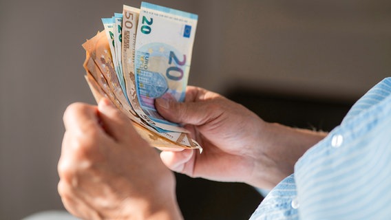 Eine männliche ältere Person hält einige Euroscheine in den Händen und scheint diese zu zählen © panthermedia.net/Westend61Premium (Arman Zhenikeyev) Foto: Westend61Premium (Arman Zhenikeyev)