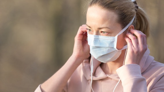 Eine Frau setzt sich eine Schutzmaske auf. © photocase Foto: kastoimages