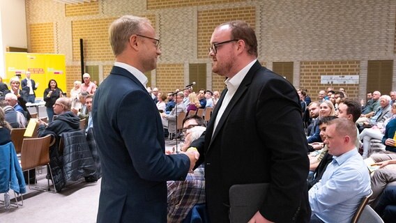 Michael Kruse (FDP, l), Landesvorsitzender der FDP in Hamburg, vollzieht einen Handschlag mit Carl Cevin-Key Coste (FDP). © picture alliance/dpa Foto: Jonas Walzberg