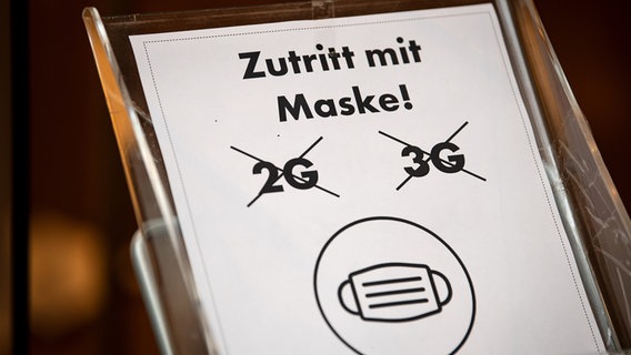 Ein Schild, auf dem 2G und 3G durchgestrichen ist, zum Tragen der Maske aber aufgerufen wird. © picture alliance / dpa Foto: Sina Schuldt