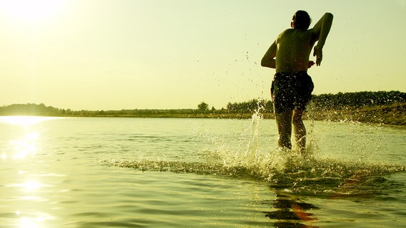 Ein Mann läuft im Gegenlicht in einen See © photocase Foto: froodmat