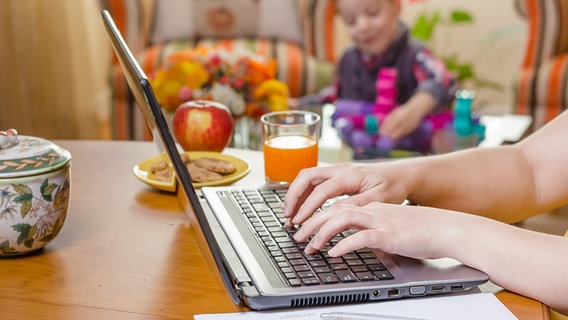 Eine Frau arbeitet zu Hause bei ihrem Kind an einem Laptop. © panthermedia Foto: doble dphoto