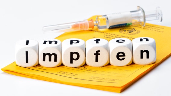 Eine Spritze liegt mit sechs Würfeln, auf denen "Impfen" steht, auf einem Impfausweis. © Colourbox Foto: Henrik Dolle