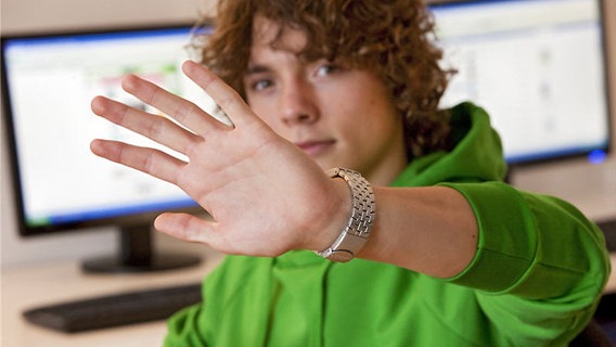Ein Jugendlicher sitzt an einem Computer und hält schützend die Hand vor sein Gesicht. © klicksafe / Uwe Völkner Foto: Uwe Völkner