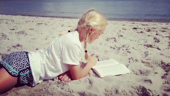 Ein Kind liegt am Strand und liest. © Katharina Mahrenholtz 