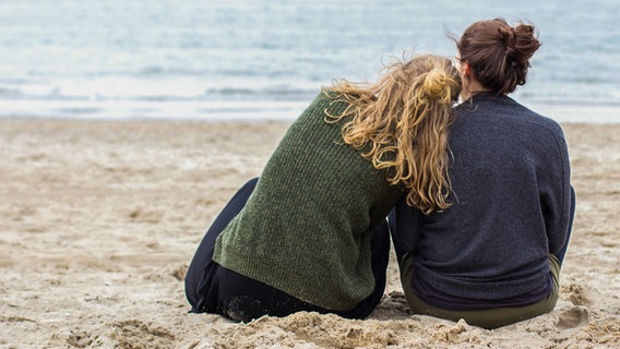 Zwei Frauen sitzen nebeneinander am Strand und schauen aufs Meer. © photocase Foto: thesunny