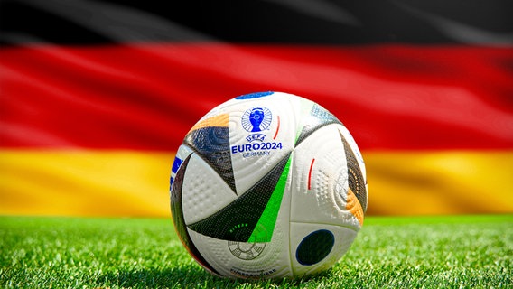 Der Fußball der EM 2024 liegt auf dem Rasen vor einer Deutschlandfahne © picture alliance / CHROMORANGE Foto: Michael Bihlmayer