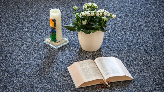 Eine Kerze und eine Blume stehen vor einer aufgeschlagenen Bibel. © Kirche im NDR/Christine Raczka Foto: Christine Raczka