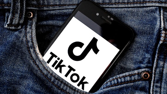 TikTok-Logo auf einem Handy, das in einer Hosentasche steckt. © picture alliance / CTK Foto: Petr Svancara