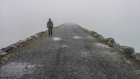 EIn Mann geht im Nebel einen Weg auf einem Damm entlang. © photocase Foto: Alpenfux