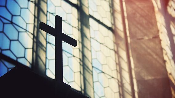 Kreuz vor einem Kirchenfenster © photocase.de Foto: claudiarndt