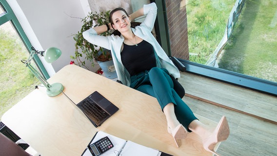 Eine Frau legt in einem Büro entspannt die Füße auf ihren Schreibtisch © picture alliance / dpa-tmn Foto: Christin Klose