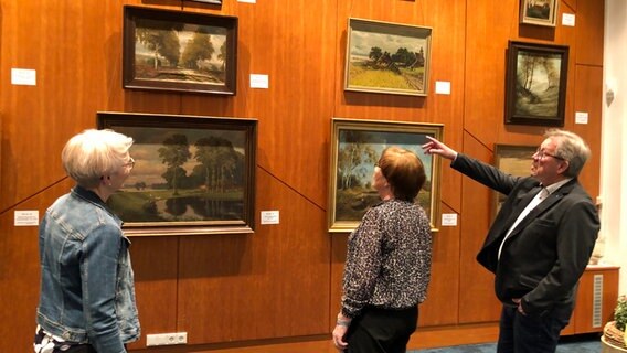 Eine Mann und eine Frau gucken sich Gemälde an, die an einer Wand hängen. © NDR Foto: Thomas Schwierzi