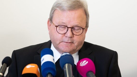 Bischof Franz-Josef Bode sitzt bei einer Pressekonferenz mit geschlossenen Augen vor Mikrofonen. © Friso Gentsch/dpa 