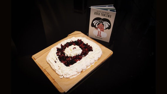 Ein Brett mit einem Baiser-Dessert (Pavlova) und einem Buch -  Folgenfoto von eat.READ.sleep © NDR Foto: Tim Piotraschke