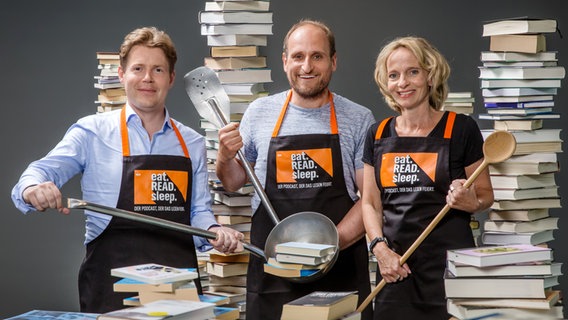 Die NDR Podcast-Hosts von eat.READ.sleep in Kochschürzen mit der Aufschrift "eat.READ.sleep" Jan Ehlert (von links), Daniel Kaiser und Katharina Mahrenholtz und Die NDR Podcast-Hosts von eat.READ.sleep in Kochschürzen mit der Aufschrift "eat.READ.sleep" Jan Ehlert (von links), Daniel Kaiser und Katharina Mahrenholtz und © NDR / Christian Spielmann Foto: Christian Spielmann