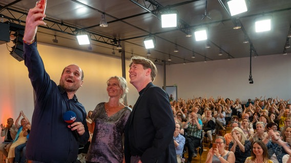 Die NDR Podcast-Hosts von eat.READ.sleep Daniel Kaiser (mit dem Handy, von links), Jan Ehlert und Katharina Mahrenholtz vor Live-Publikum in München © NDR / Catherina Hess Foto: Catherina Hess