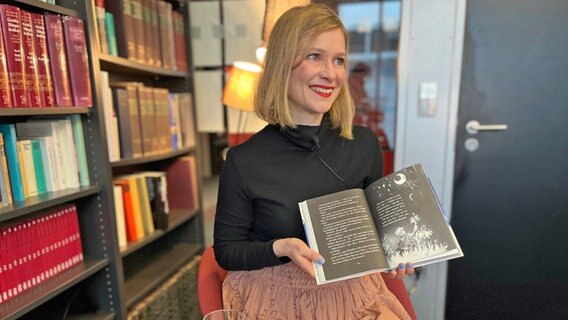 Eine Frau mit kinnlangen Haaren und schwarzem Pulli hält lächelnd ein Kinderbuch in der Hand - (Autorin Claudia Scharf mit ihrem Buch zu Besuch beim NDR) © NDR Foto: Patricia Batlle