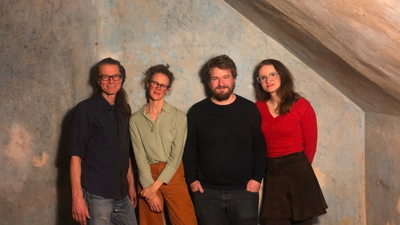 Zwei Frauen und Männer stehen lächelnd vor einer Wand. © NDR Foto: Mikko Haiko