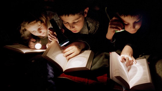 Kinder lesen mit Taschenlampen im Bett © picture alliance Foto: JOKER