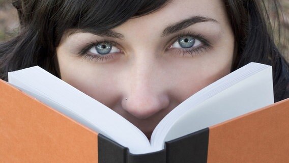 Frauengesicht schaut hinter einem aufgeschlagenen Buch hervor. © Fotolia.com Foto: Jason Stitt