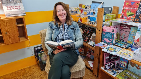 Maria Glusgold sitzt mit einem Buch auf dem Schoß auf einem Sessel und lächelt in die Kamera. © NDR Foto: Agnes Bührig