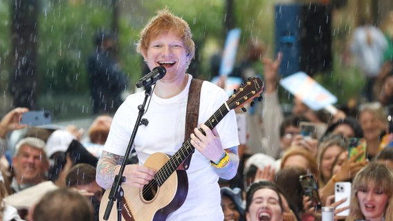 Musiker Ed Sheeran steht im Regen auf einer Bühne und singt zur Gitarre. © IMAGO / UPI Photo 