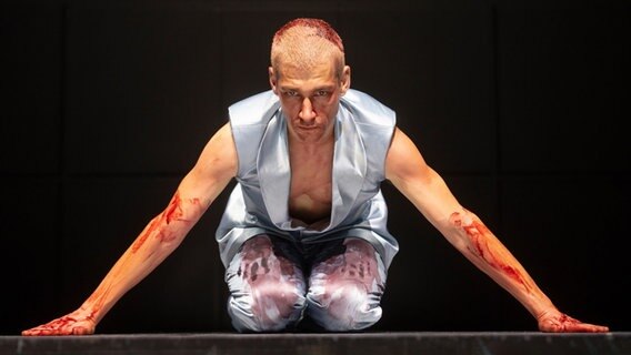 Ein Mann mit kunstblutverschmierter Kleidung stützt sich auf einen Bühnenboden. © Silke Winkler Foto: Silke Winkler