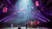 Eine Gruppe von Personen auf einer Bühne, über ihnen schweben verschiedene Gegenstände © Schauspiel Hannover / Katrin Ribbe Foto: Katrin Ribbe