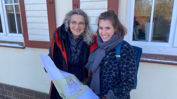 Zwei Frauen stehen mit einem Dokument vor einem Haus. © NDR Foto: Andrea Schwyzer